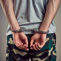 Handcuffed wrists in gray T-shirt and camouflage pants, neutral background implies custody For Social Media Post Size photo