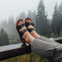 Feet in black sandals resting on railing, misty forest backdrop suggests tranquility For Social Media Post Size photo