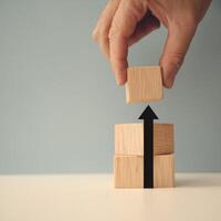 Hand places block atop stack with arrow pointing up, blue background emphasizes growth For Social Media Post Size photo