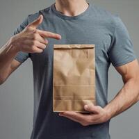 Man in gray shirt pointing at brown paper bag, neutral background focus For Social Media Post Size photo
