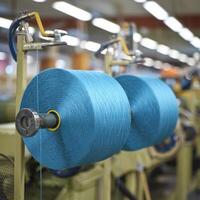 Spools of blue thread connected to machinery in busy textile workshop environment For Social Media Post Size photo