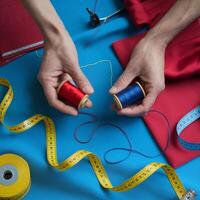 Hands hold thread spools, measuring tape on colorful blue fabric For Social Media Post Size photo