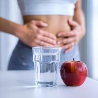 Person touches abdomen, water and apple focus on hydration and well being For Social Media Post Size photo