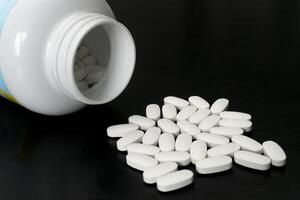 White tablets spilled from a bottle on a black surface photo