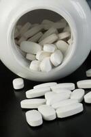 Pills are spilling out of a white container on a dark surface photo