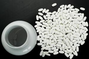 White tablets spilled from a container on dark surface photo