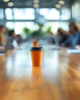 A bright orange coffee cup stands alone on a table surrounded by people deep in discussion photo