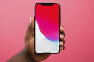 A dark skinned hand holds a smartphone showcasing a dynamic iOS wallpaper against a pink background photo