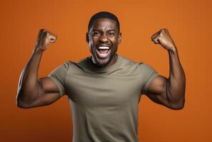 A dark skinned man with muscular arms raises his fists in a triumphant pose against an orange background photo