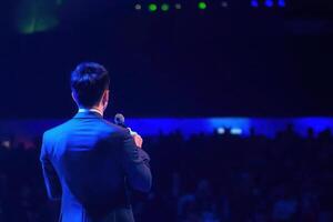 Speaker addressing large audience conference event presentation business meeting microphone man photo
