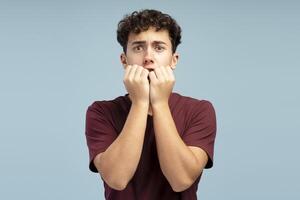 Scared shocked boy, pupil wearing red t shirt looking at camera standing isolated on blue background photo