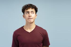 Portrait of scared worried teen boy looking away on copy space, standing isolated on blue background photo