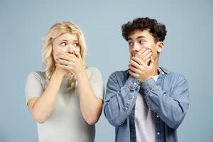Scared, young boyfriend and girlfriend covering mouth with hands, looking each other photo