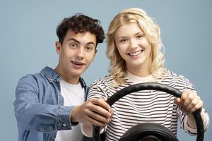 Happy, attractive couple together learning to drive, holding helm isolated on blue background photo