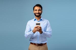 Portrait of smiling, happy bearded middle aged Indian man holding mobile phone, using mobile app photo
