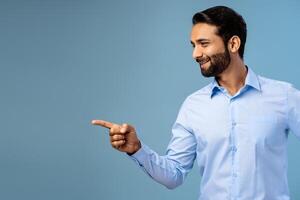 Smiling, happy, bearded middle aged Indian man pointing finger on copy space photo