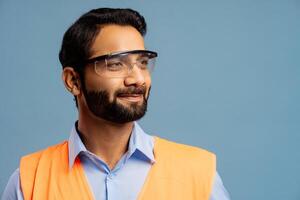 Successful Indian man wearing orange vest and protective eyeglasses looking away on cop space photo