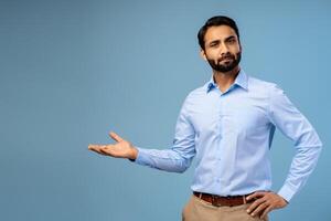 Portrait of serious, pensive middle aged Indian man showing with hand on copy space photo