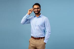Handsome, bearded Indian businessman wearing stylish eyeglasses, posing isolated on blue background photo
