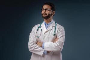 Smiling Indian man, doctor wearing stylish eyeglasses, white coat with crossed arms looking away photo