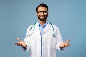 Smiling bearded Indian man, doctor wearing white coat with stethoscope, eyeglasses explaining photo