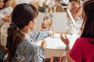 Close-up of young women in casual clothes at a painting workshop. Friends at a table with easels and blank canvases. The view from the back. photo