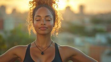 A woman enjoys a moment of mindfulness as the sun sets in the background. She is outdoors, surrounded by an urban landscape, and appears serene and focused. photo