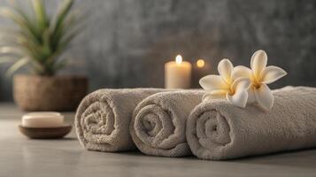 Soft towels are neatly rolled and placed alongside a soothing candle and a beautiful flower. photo