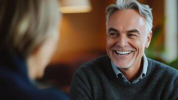 A dentist, with a friendly smile and gray hair, engages in a pleasant conversation with a patient in a comfortable clinic. The atmosphere is warm and inviting, promoting relaxation. photo