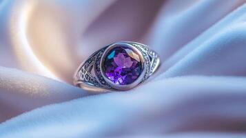 A silver ring with an intricate design showcases a stunning purple gemstone at its center. The ring is delicately placed on soft, silky fabric, enhancing its elegance and charm. photo
