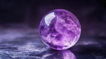 A stunning purple gemstone orb sits elegantly on a dark reflective surface. The orb showcases intricate internal patterns and shimmering facets that catch the light beautifully. photo