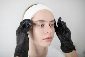 In a beauty salon, a woman undergoes a permanent makeup procedure, with an expert carefully threading her eyebrows. The relaxing atmosphere enhances the pampering experience. photo