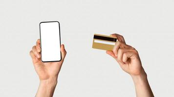Online shopping concept. Unrecognizable man holdng credit card and smartphone with empty screen on white background, space for design. Panorama photo