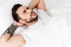 Angry young man unable to sleep, having insomnia, lying in bed and looking up, copy space. Mental health problem, male depression and sleeplessness concept photo