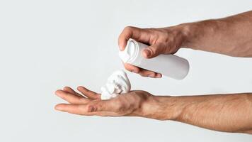 Unrecognizable man applying shaving foam from bottle onto his hand, white background. Panorama photo