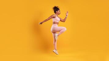A woman in athletic attire exercises with enthusiasm against a bright yellow backdrop. She focuses on her fitness routine, showcasing strength and determination. photo
