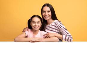 A mother and her teenage daughter share a joyful moment, smiling and embracing each other. The cheerful atmosphere is enhanced by the bright yellow background that surrounds them. photo