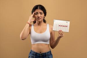 A young Indian woman shows concern while holding a calendar with marked dates, have menstruation delay photo