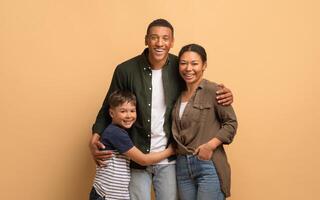 A loving African American family shares a warm embrace, with a father, mother, and son smiling joyfully against a neutral background. Their bond reflects happiness and togetherness. photo