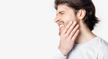 Not tolerate pain in teeth and dentures. Man suffers from pain and presses his hand to cheek, panorama, cropped, studio shot photo