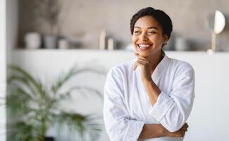 A woman wearing a white bathrobe stands in her modern living space, smiling and looking relaxed. Soft light filters through the room, creating a calm atmosphere perfect for self-care, copy space photo