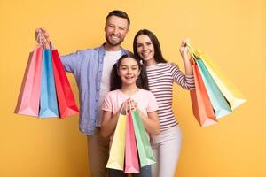 A cheerful family consisting of a mother, father, and teenage daughter poses happily, holding colorful shopping bags. They display love and connection in a vibrant setting. photo