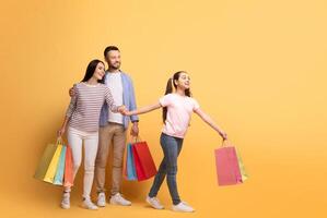 A happy family of three, including a mother, father, and teenage daughter, share smiles while shopping. The daughter leads with colorful bags, showcasing family bonding and affection, copy space photo