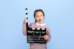 A joyful girl expresses excitement while holding a clapperboard, indicating her role in a creative project. The setting is bright and isolated, enhancing her joyful demeanor. photo