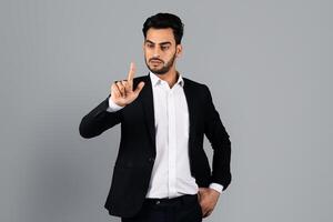 A Middle Eastern businessman stands in a well-lit studio, making a hand gesture that conveys authority. Dressed in a sleek suit, he exudes confidence and professionalism in a corporate lifestyle. photo