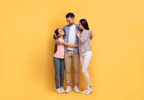 A loving family of three, consisting of a father, mother, and teenage daughter, share warm embraces and smiles. They stand closely together, radiating affection in a cheerful setting. photo