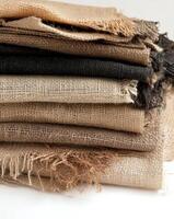 Stack of various textured burlap fabrics in neutral tones displaying woven patterns photo