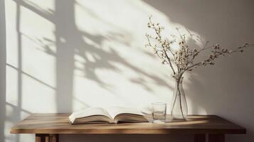 Sunlit minimalist table with open book, glass vase of flowers, and shadows photo