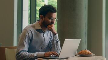 Arabian Indian man typing laptop keyboard concentrated business guy male businessman at cafe table online work computer browsing internet write tasks thinking freelancer manager employee distant study photo