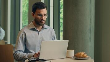 Arabian Indian man typing laptop keyboard concentrated business guy male businessman at cafe table online work computer browsing internet write tasks thinking freelancer manager employee distant study photo